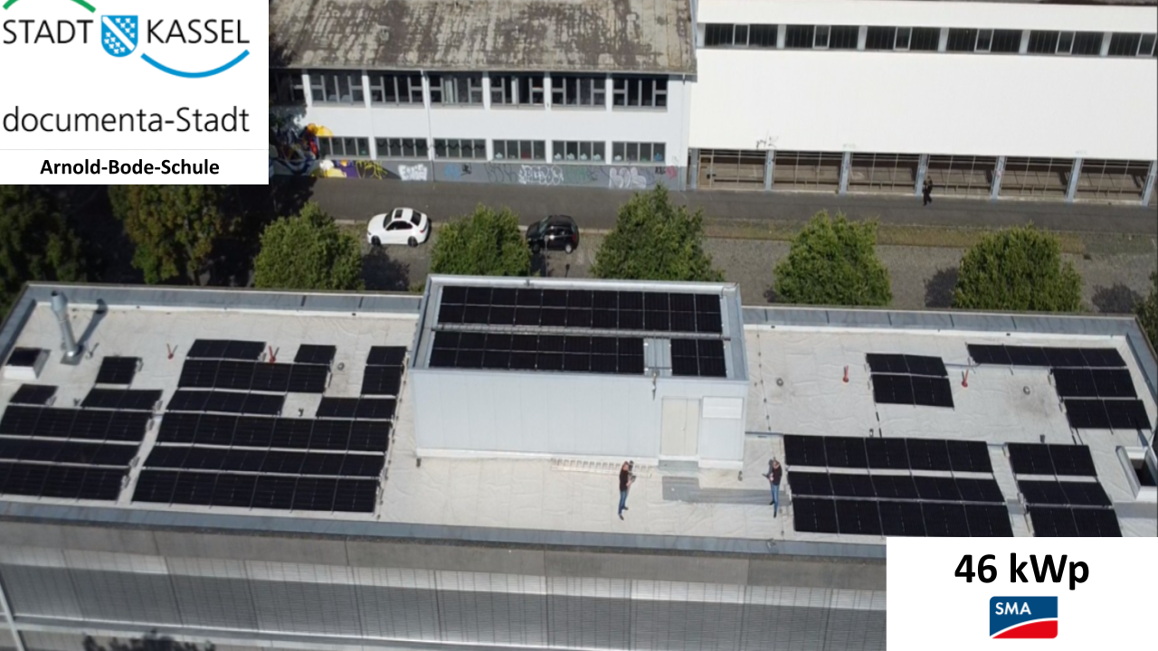 Zwei Personen stehen entspannt auf einem Flachdach mit zahlreichen Solarpanels in der Sonne