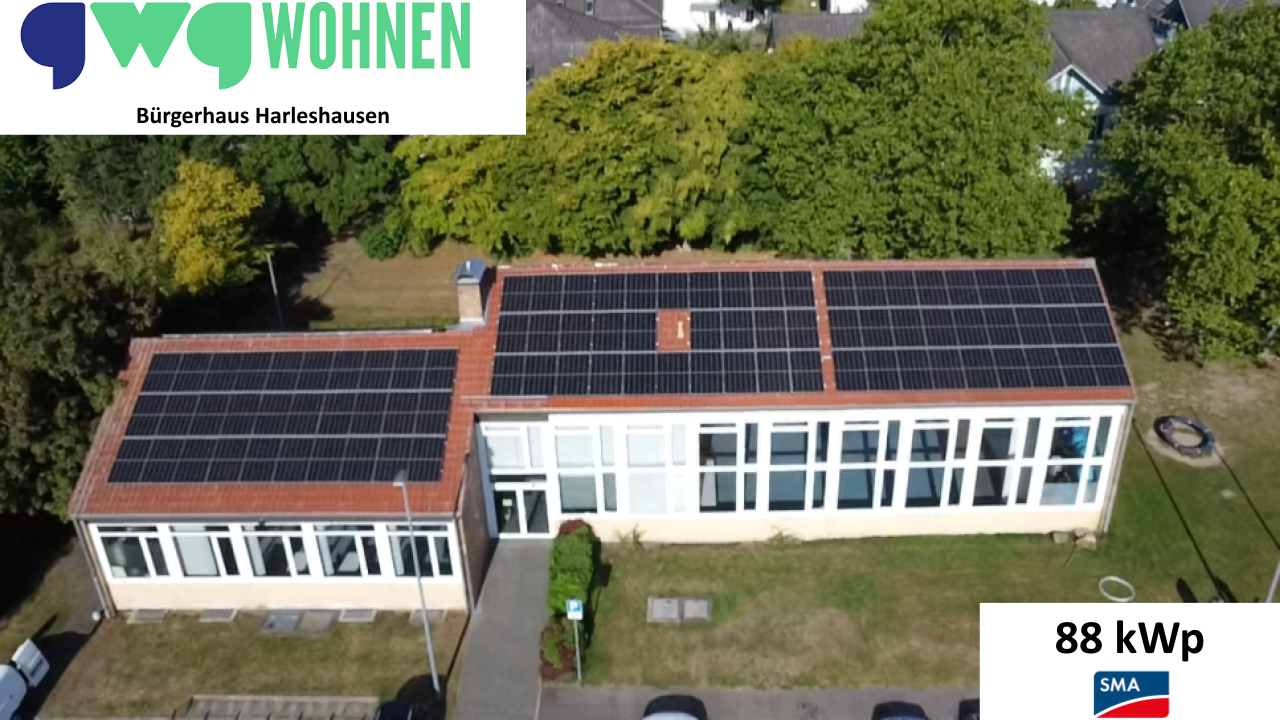 Ein langes Gebäude mit vielen Fenstern und großen schwarzen Solarmodulen auf dem Dach