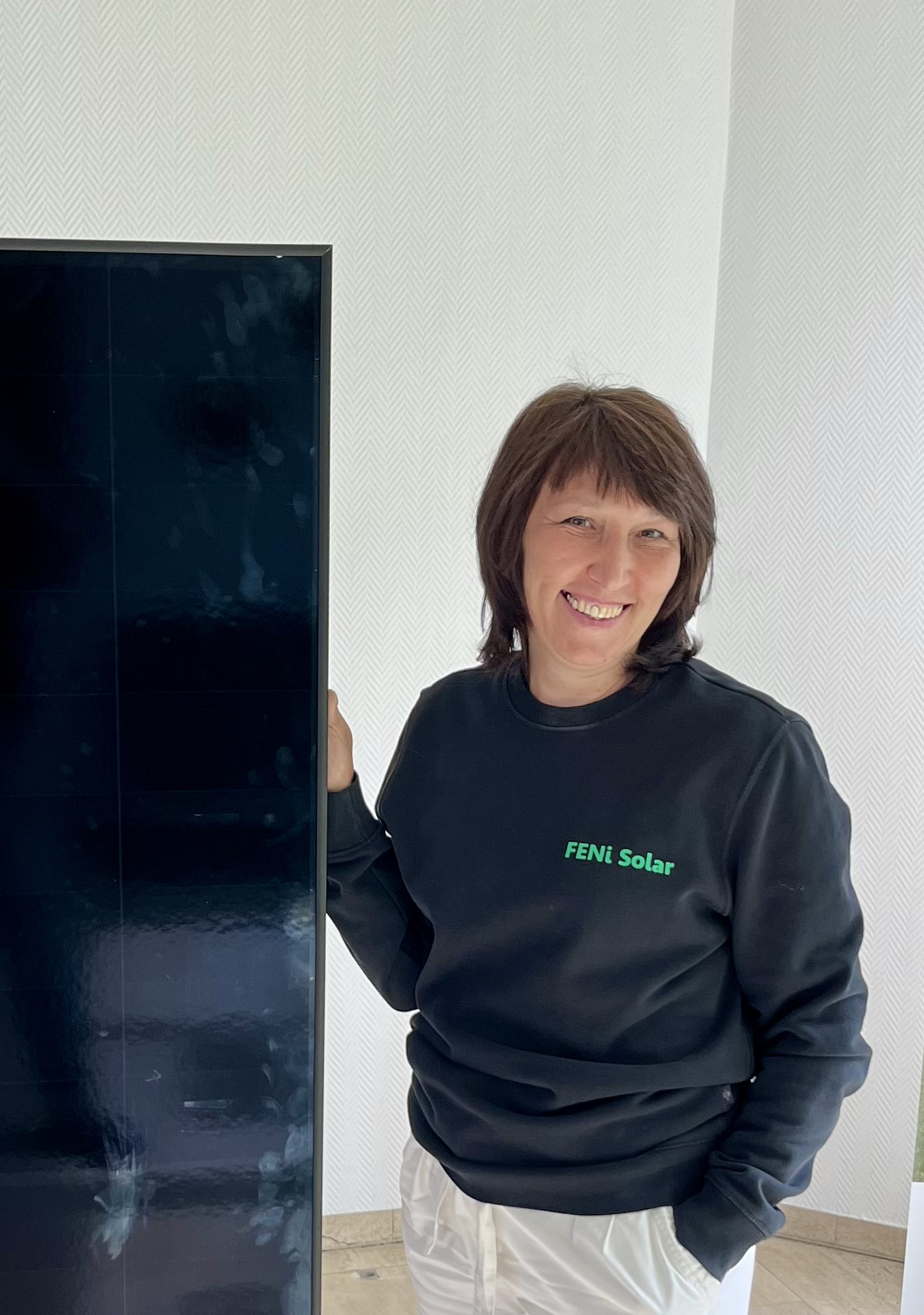 Person mit neutralem Blick in schwarzem Pullover neben Fernseher